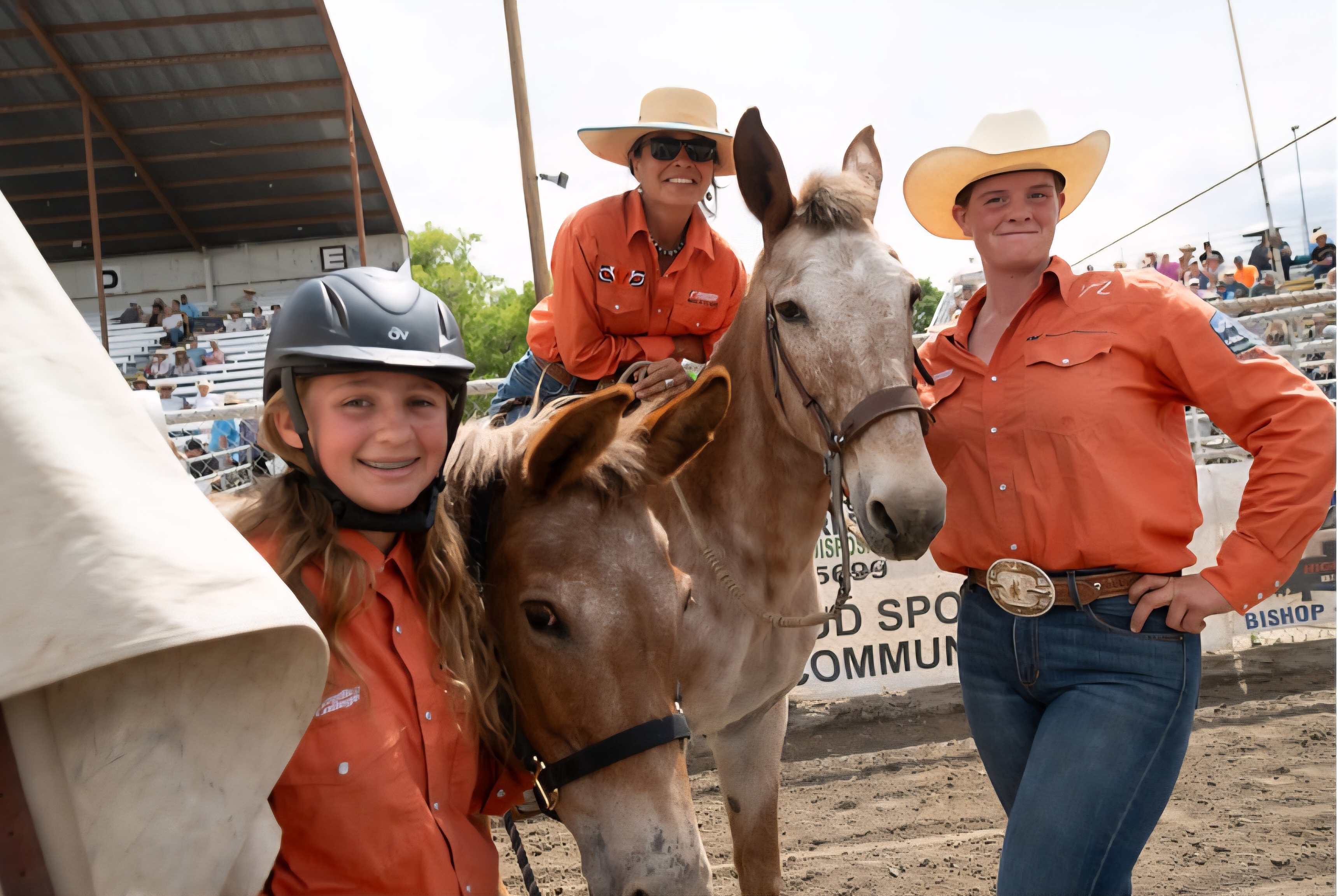 Three women in cowboy hats pose with horses at a rodeo event, showcasing a spirit of camaraderie and equestrian culture.