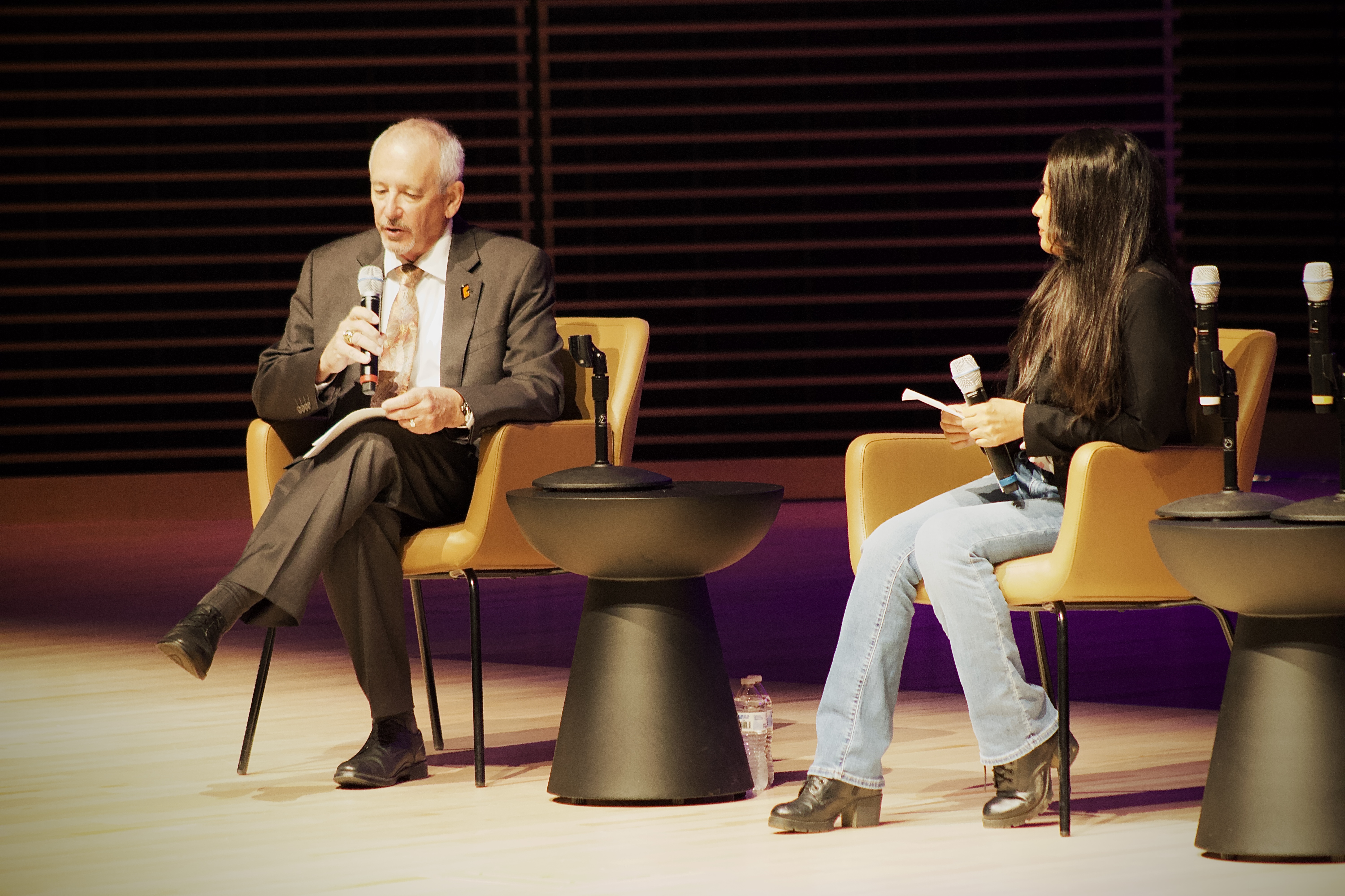 Dr Buckley speaks into a microphone while seated next to a woman in casual attire, both participating in a discussion on a stage.